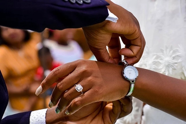 Bride helping groom put on his watch during wedding preparation inside wedding tent